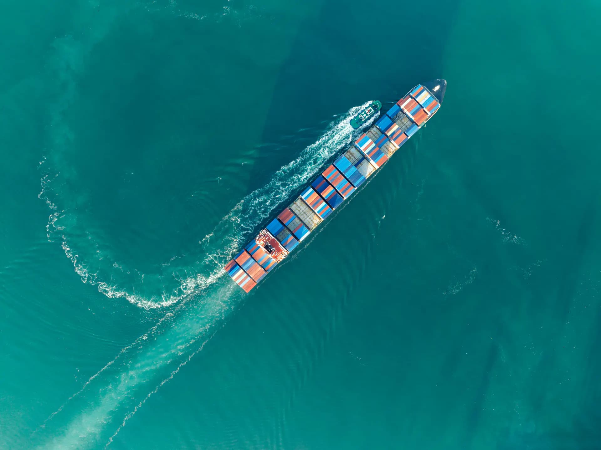 Aerial view of a container ship under way at sea, a pilot boat drawing alongside as it approaches port.