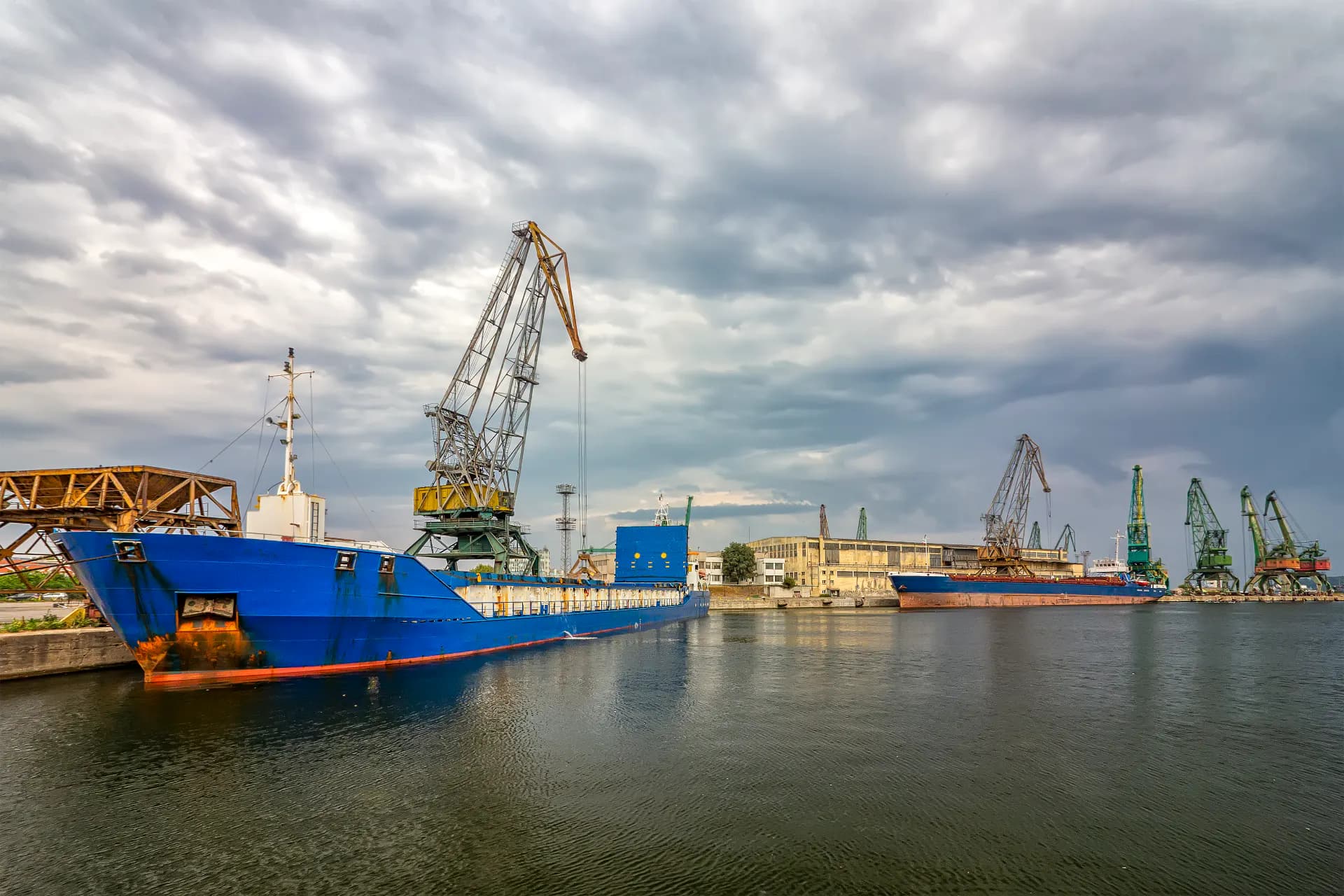 Cargo vessel alongside a working port under cloudy skies