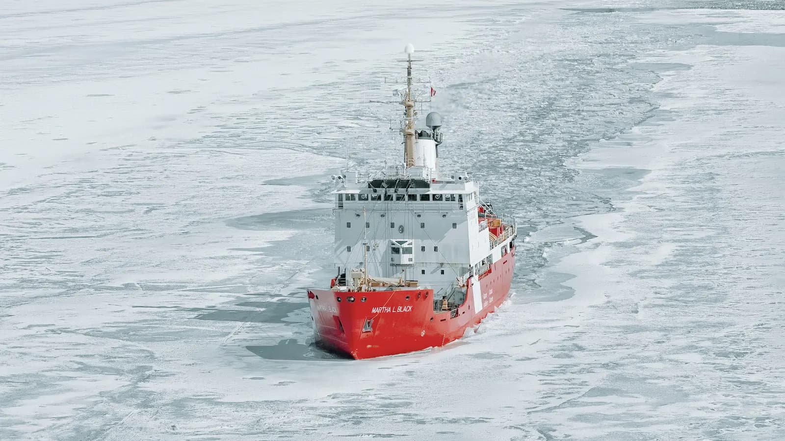 Red and white icebreaker cutting through sea ice