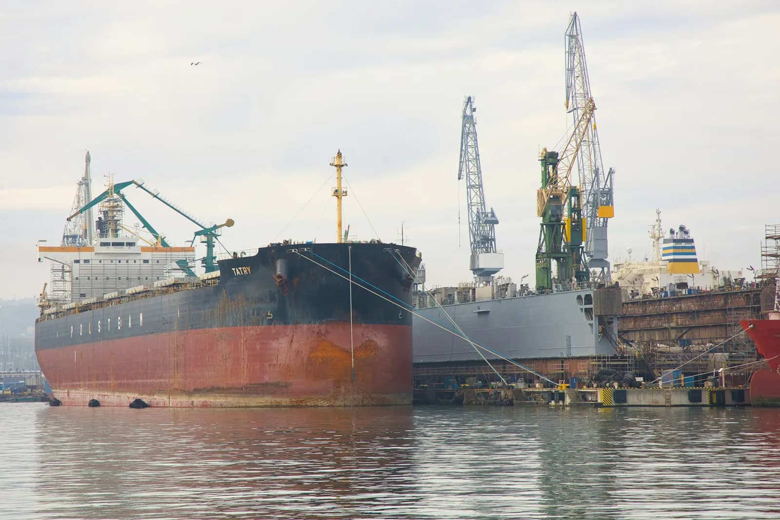 Ship docked at a shipyard with cranes overhead