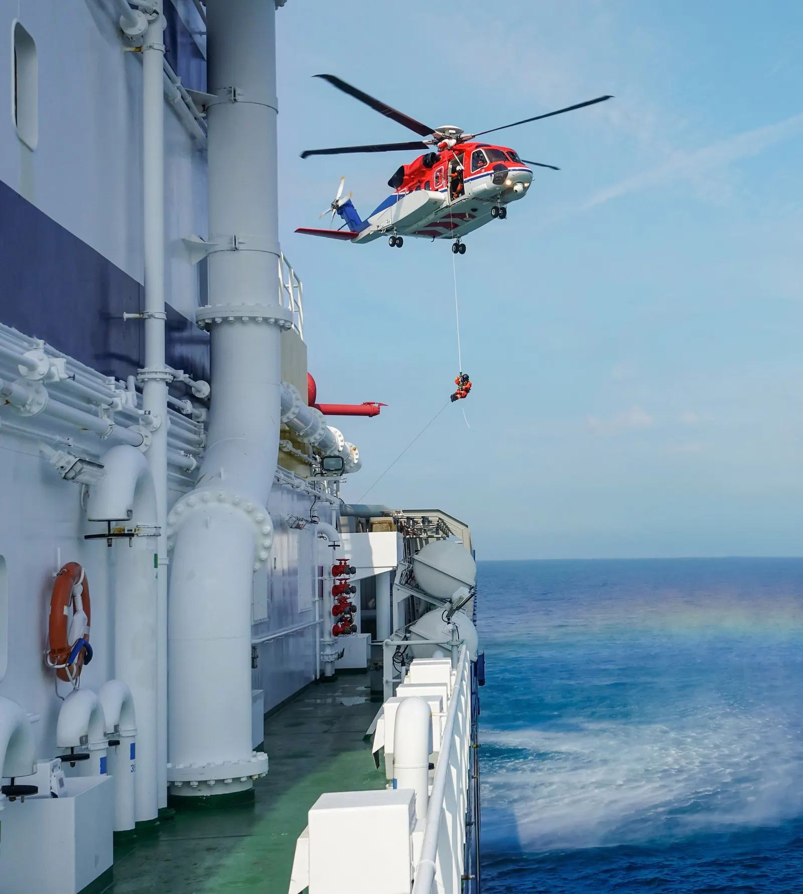 Rescue helicopter winching a crewman to a ship at sea