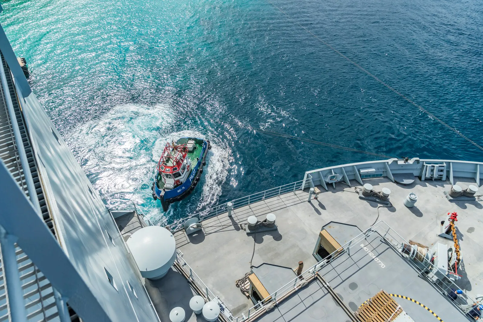 A small boat approaching a larger vessel at sea, seen from the ship