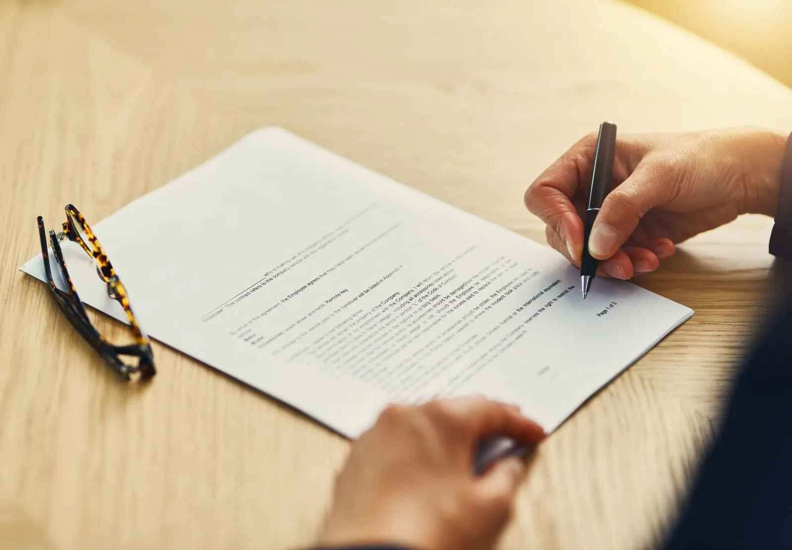 A hand signing a contract on a desk