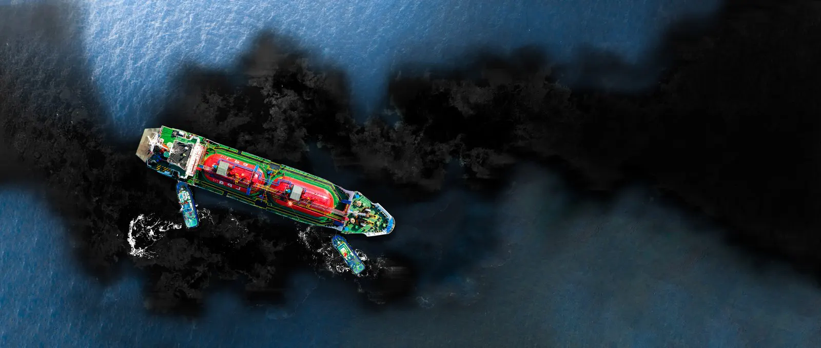 Tanker surrounded by dark oil on the sea surface seen from above